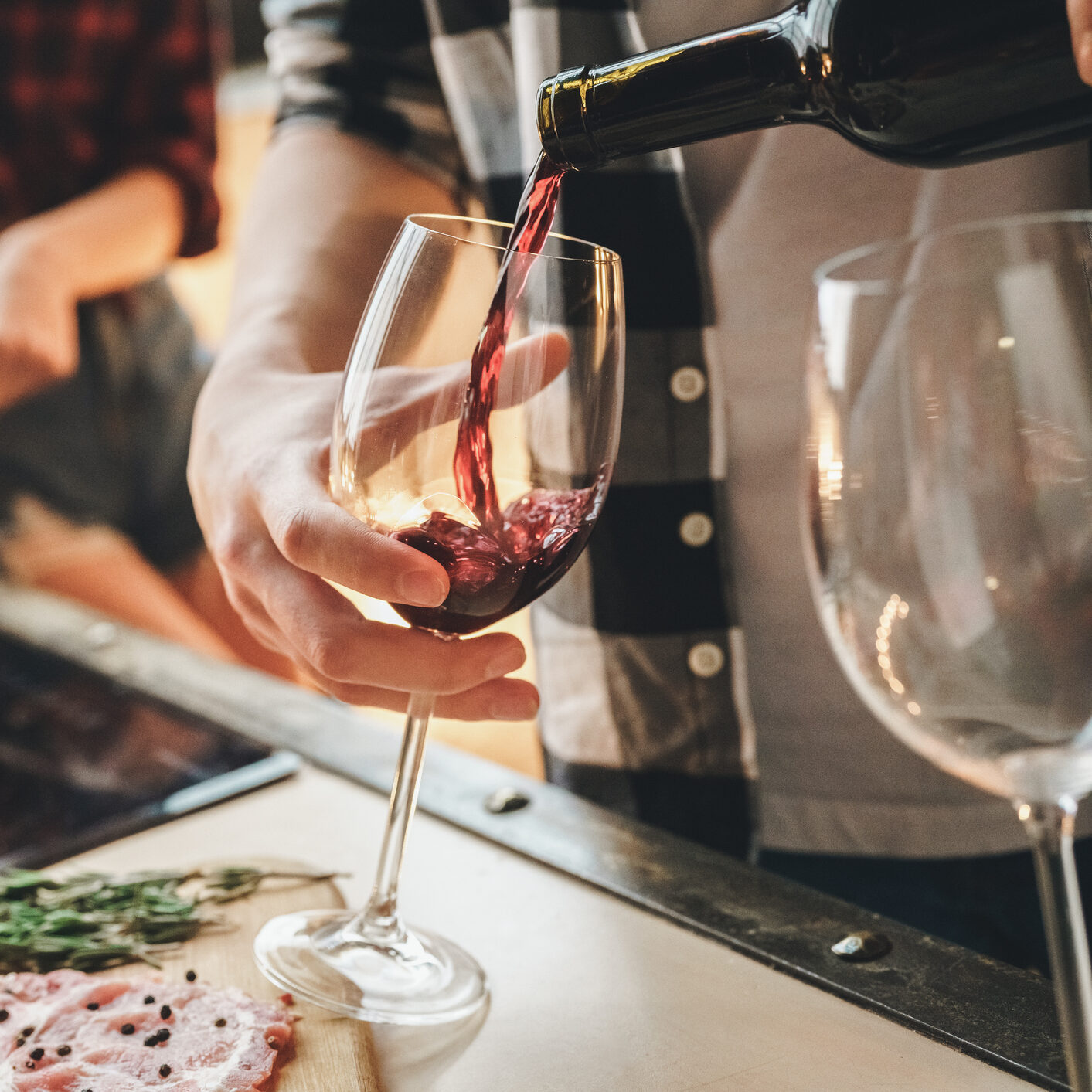 Closeup shot of a hand pouring red wine into a wine glass from a wine bottle.