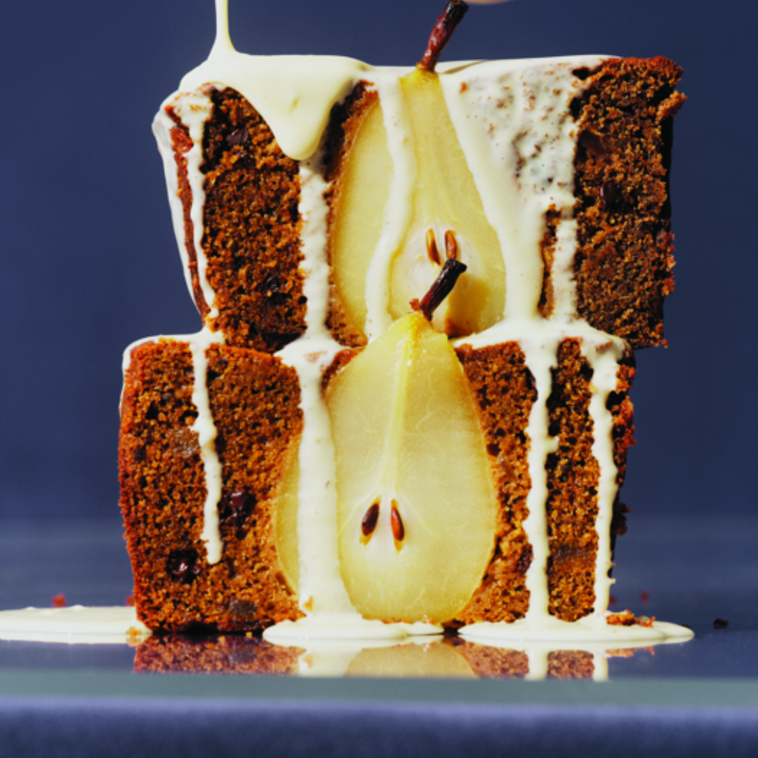 Two slices of brown loaf cake with half a pear inside being drizzled with runny white sauce.
