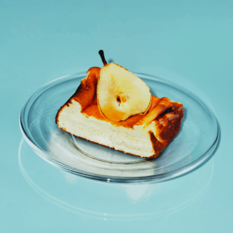 A slice of basque cheesecake topped with a poached pear on a clear plate.