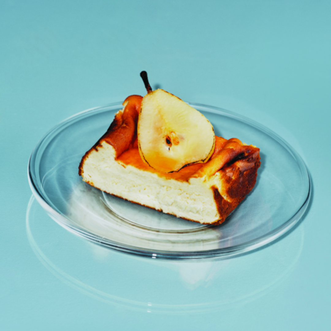 A slice of basque cheesecake topped with a poached pear on a clear plate.