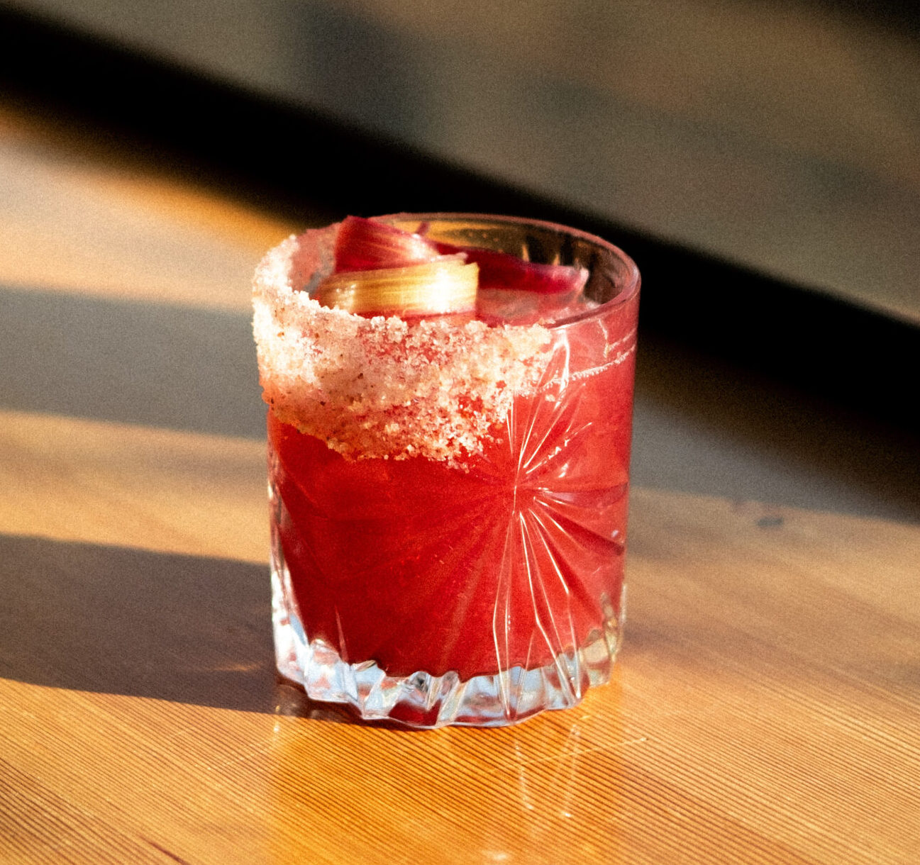 A red rhubarb margarita in a salt-rimmed glass garnished with a rhubarb swirl.