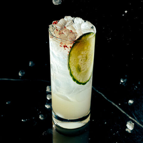 A margarita in a Collins glass with a slice of cucumber and topped with gochugaru powder.