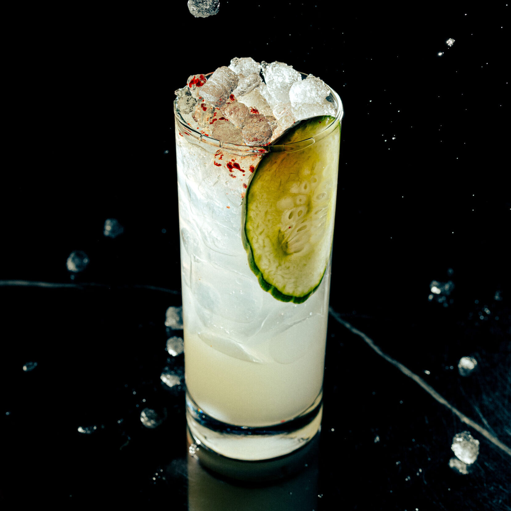 A margarita in a Collins glass with a slice of cucumber and topped with gochugaru powder.