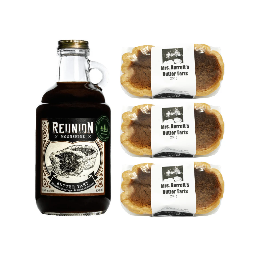 A bottle of brown moonshine next to six butter tarts packaged up in pairs.