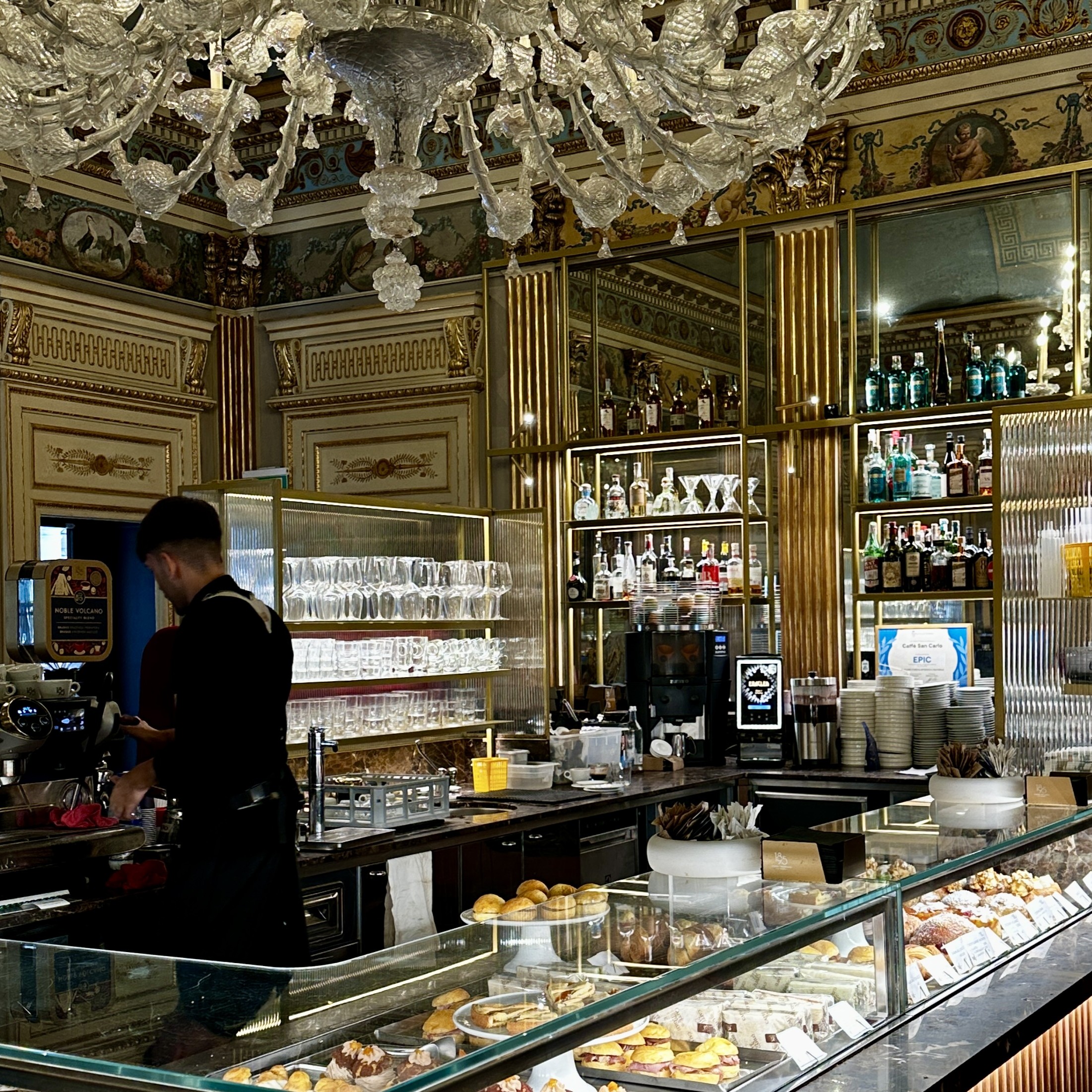 A chandelier hanging over a glass case filled with pastries in a cafe.