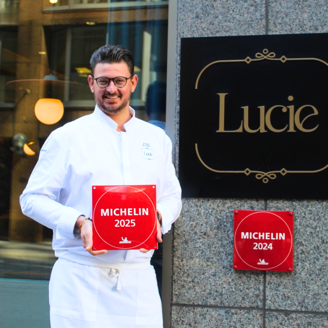 Chef Arnaud BLoquel standing in front of Michelin-recommended restaurant lucie holding the re michelin sign