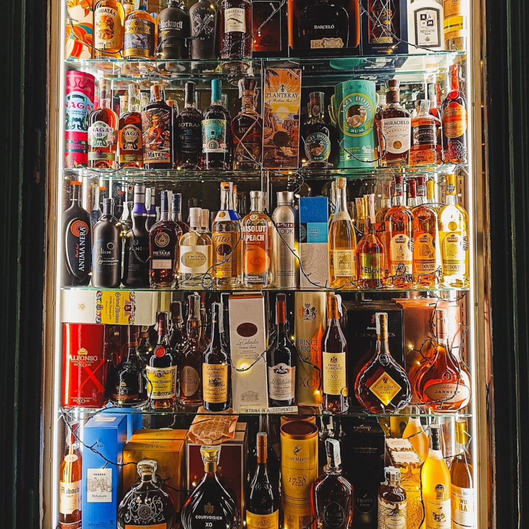 Glass case filled with colorful bottles of wine and spirits under Piazza della Repubblica porticos — historic wine shop display in Turin.