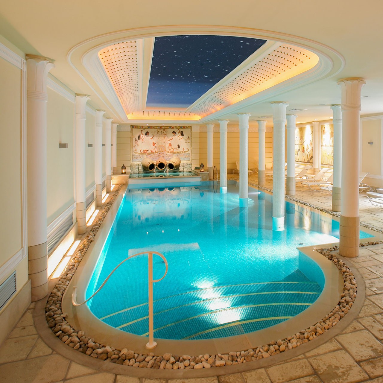 Blue-tiled indoor pool surrounded by white columns and mosaic decor — inviting spa-style hotel amenity in Turin.