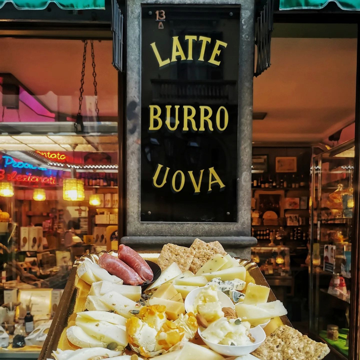 Wooden cheese board held in hand in front of a store sign reading 'Latte Burro Uova' — artisanal cheese shop showcasing regional cheeses in Turin.