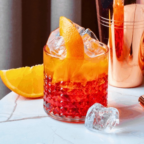 Negroni Sbagliato cocktail in a rocks glass with ice, garnished with an orange slice, made with Folonari Prosecco, Campari, and sweet vermouth.