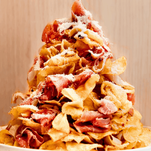 Layers of crispy kettle-cooked potato chips are stacked with torn prosciutto, drizzled with hot honey, and finished with a shower of freshly grated Parmesan.