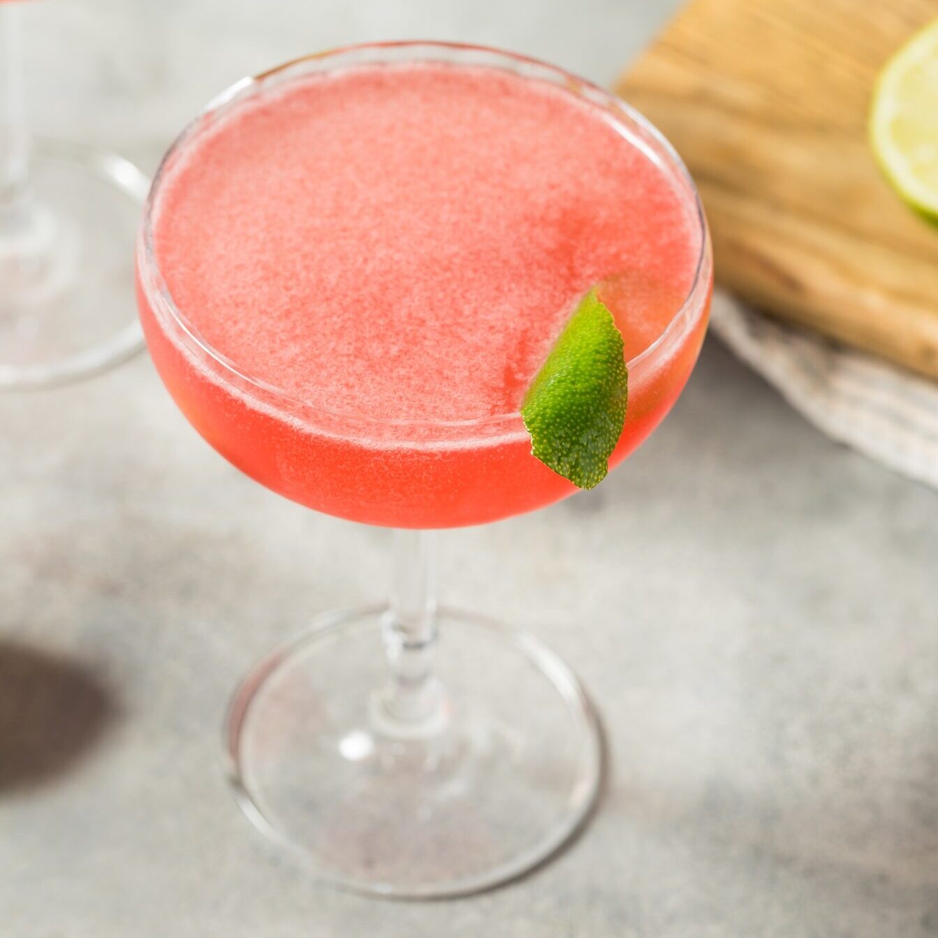 A glass filled with a pink cocktail and garnished with a leaf. 