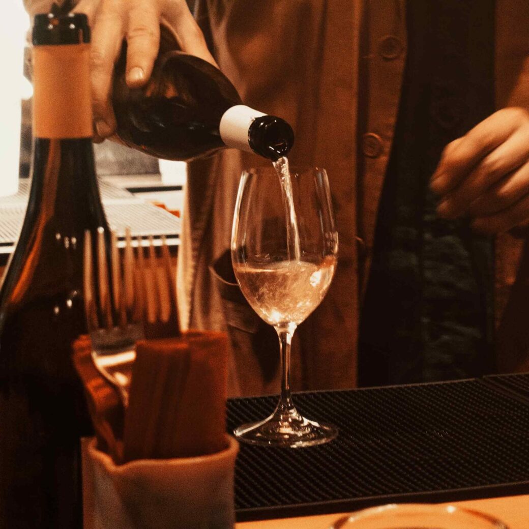 Hand pouring a bottle of sparkling wine into a glass — representing aperitivo or wine bar experience in Turin.