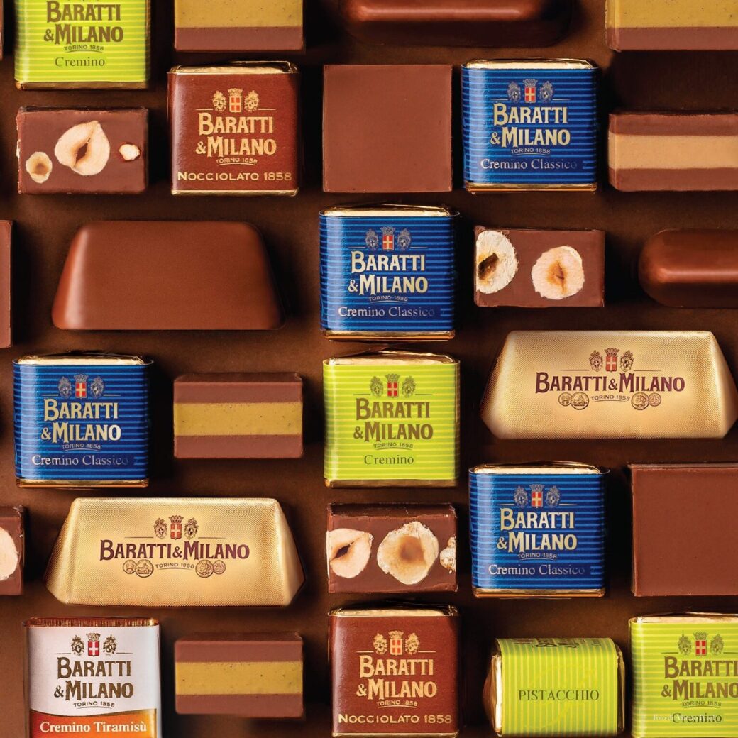 Assorted gianduiotti and chocolates — neatly wrapped and unwrapped, displayed on a tile-patterned brown background.