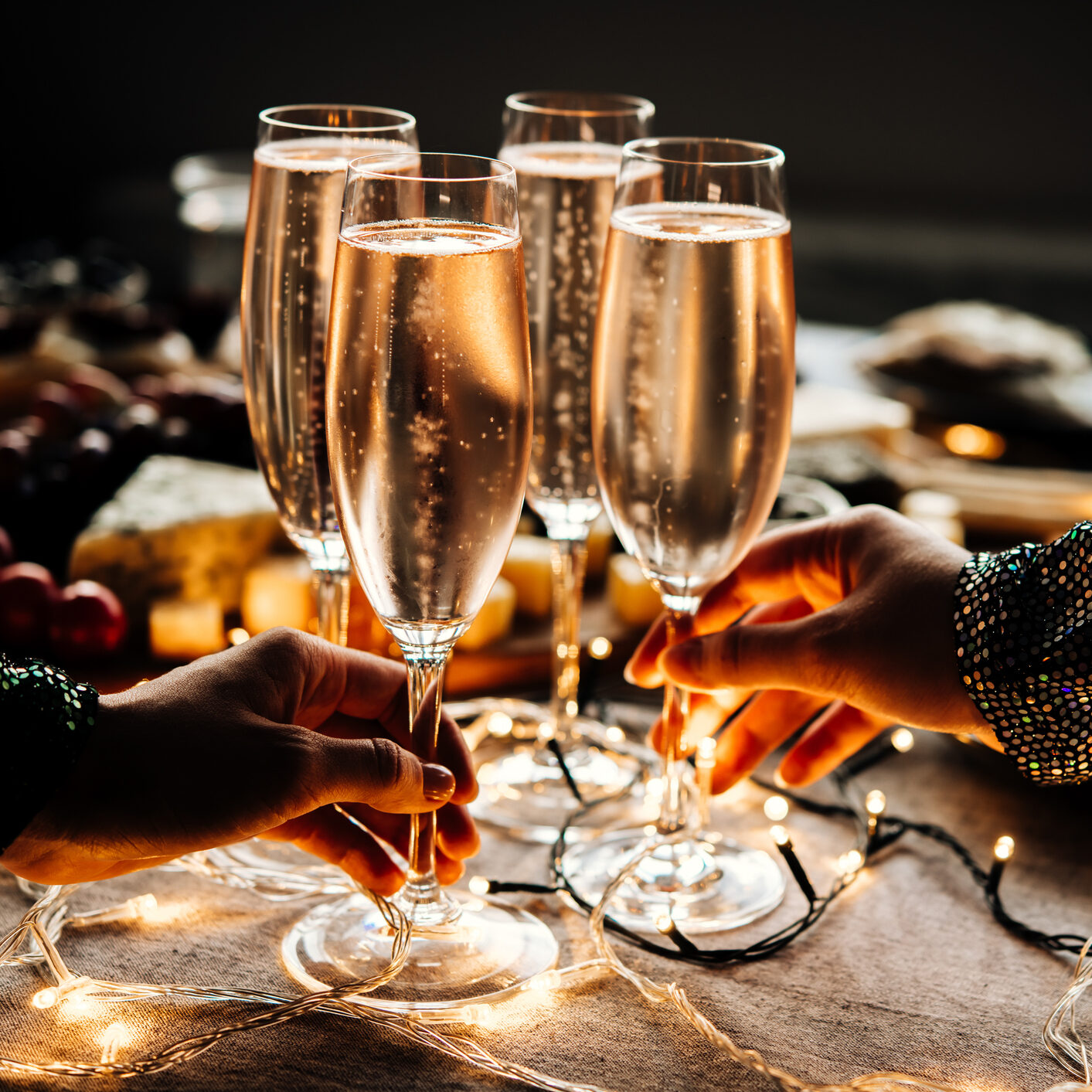 Four glasses of champagne clinking together over a darkly lit table.