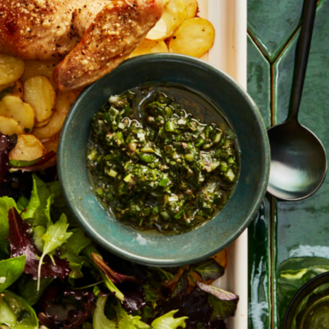 Bowl of tarragon green onion salsa verde on a tray next to potatoes and arugula.